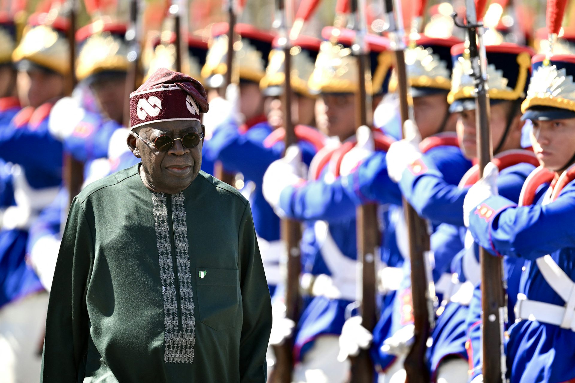 A man in traditional dress walking past men in ceremonial military dress 