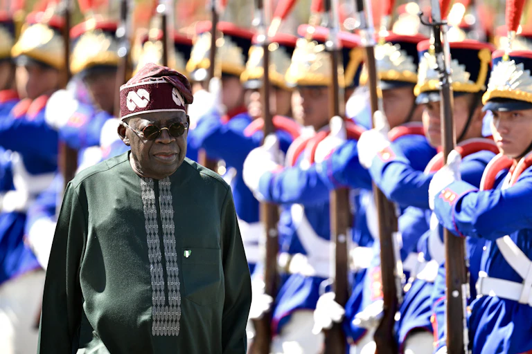 A man in traditional dress walking past men in ceremonial military dress