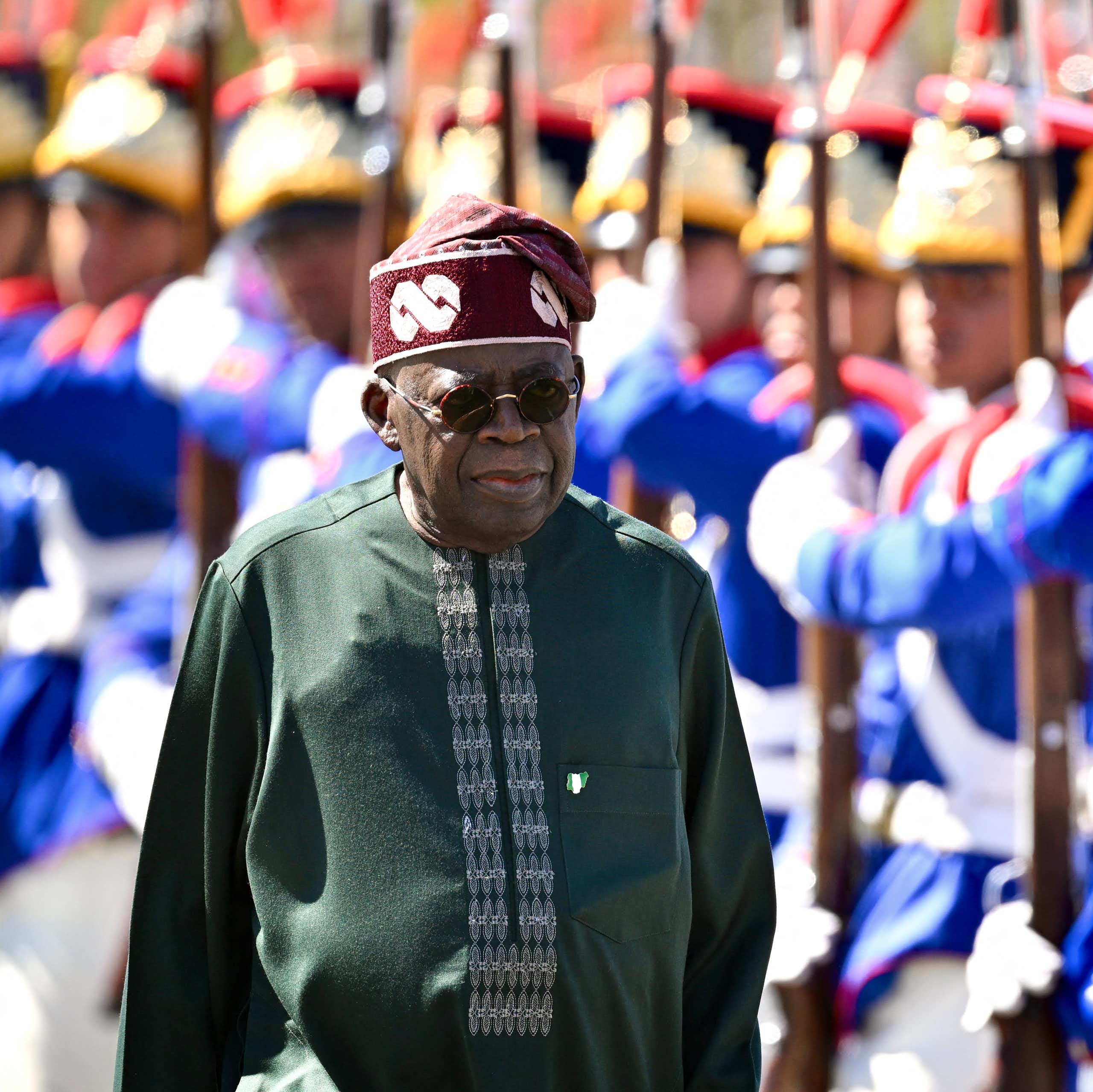 A man in traditional dress walking past men in ceremonial military dress