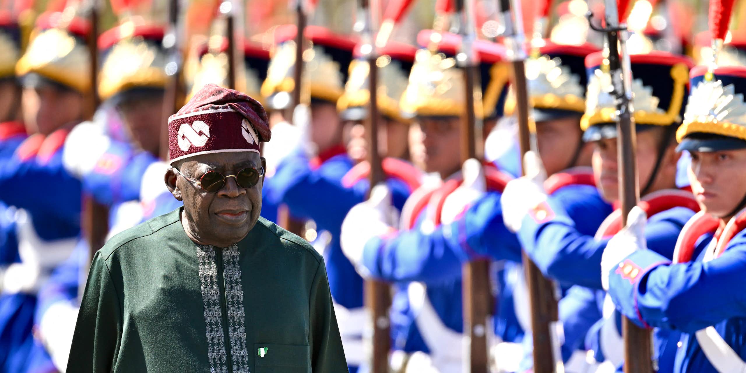 A man in traditional dress walking past men in ceremonial military dress