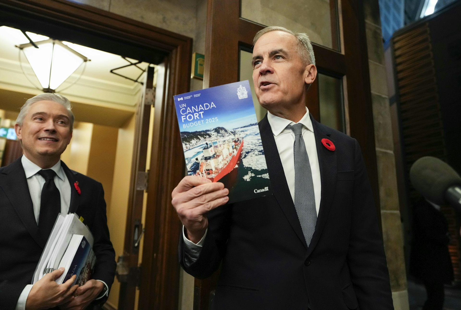 A middle-aged white man holds up a pamphlet that says 'Canada Strong Budget 2025' on it