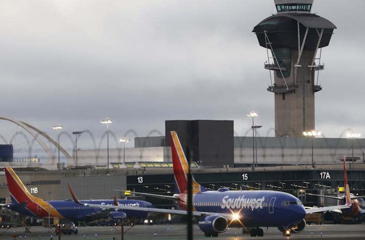 What to understand as masses of flights are grounded throughout the United States – an air trip professional explains 1 A large building is seen behind a blue plane.