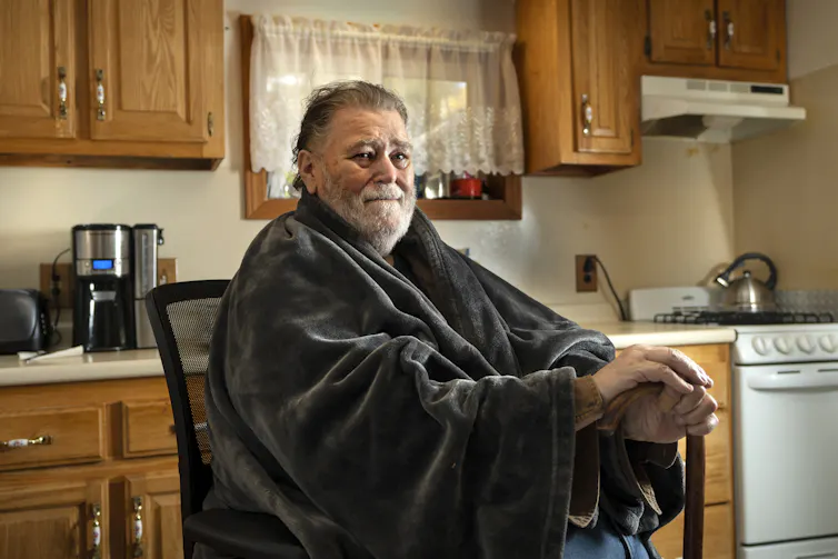 An older man wearing a shawl in his kitchen.