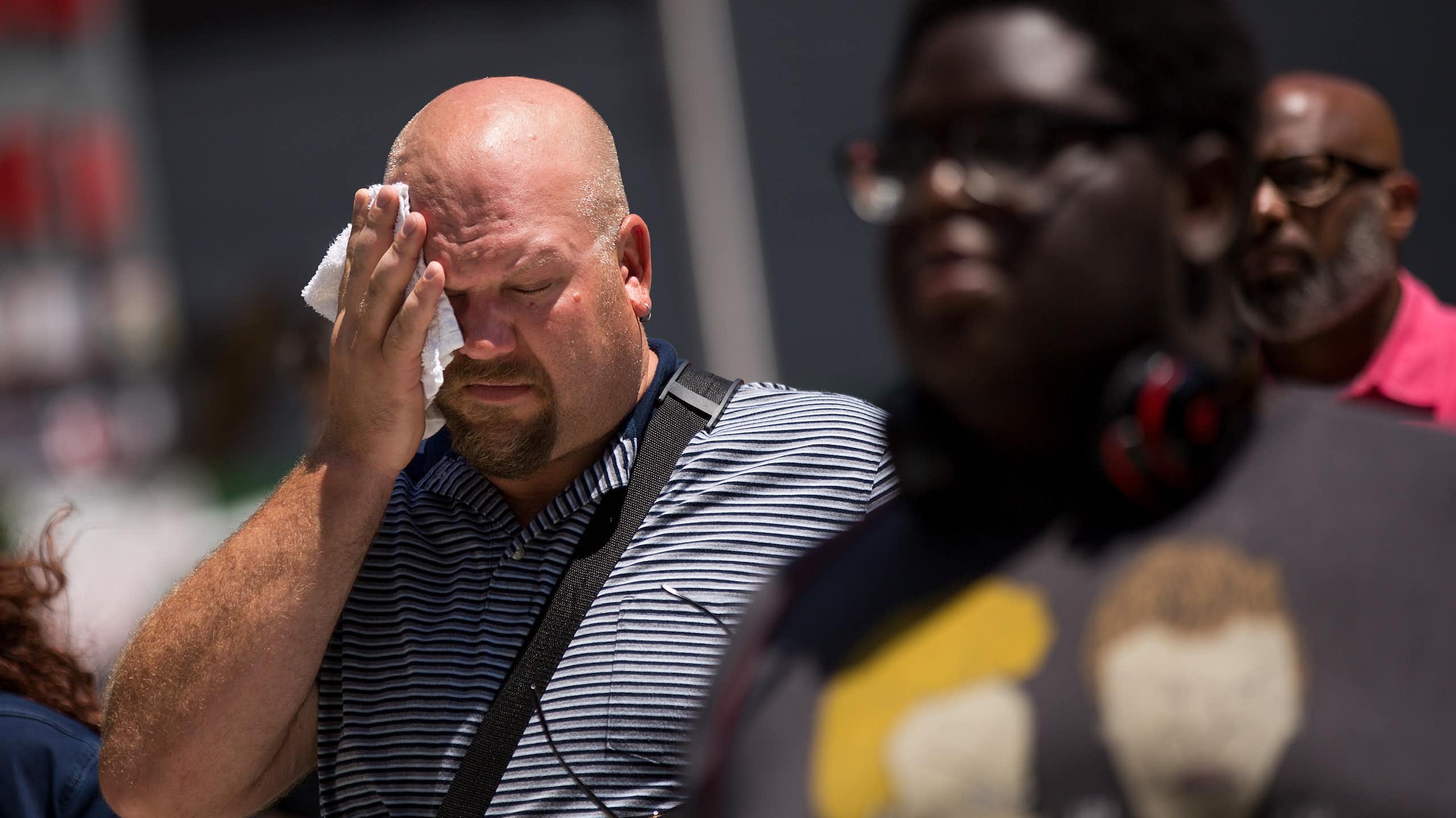 A man walking on a sidewalk wipes his forehead on a hot day.