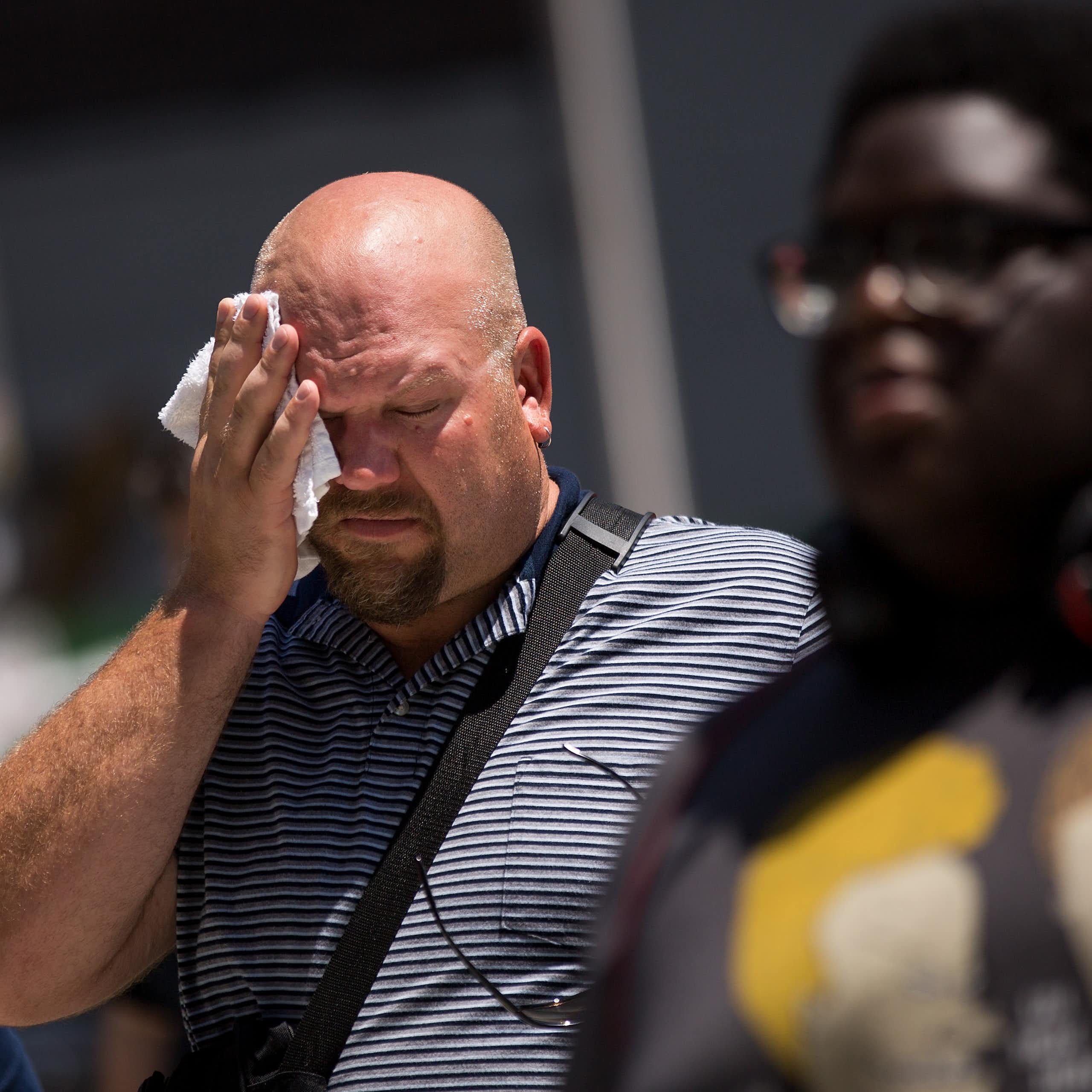A man walking on a sidewalk wipes his forehead on a hot day.