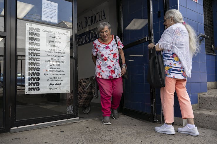 A older man holds a door for a woman at a cooling center.