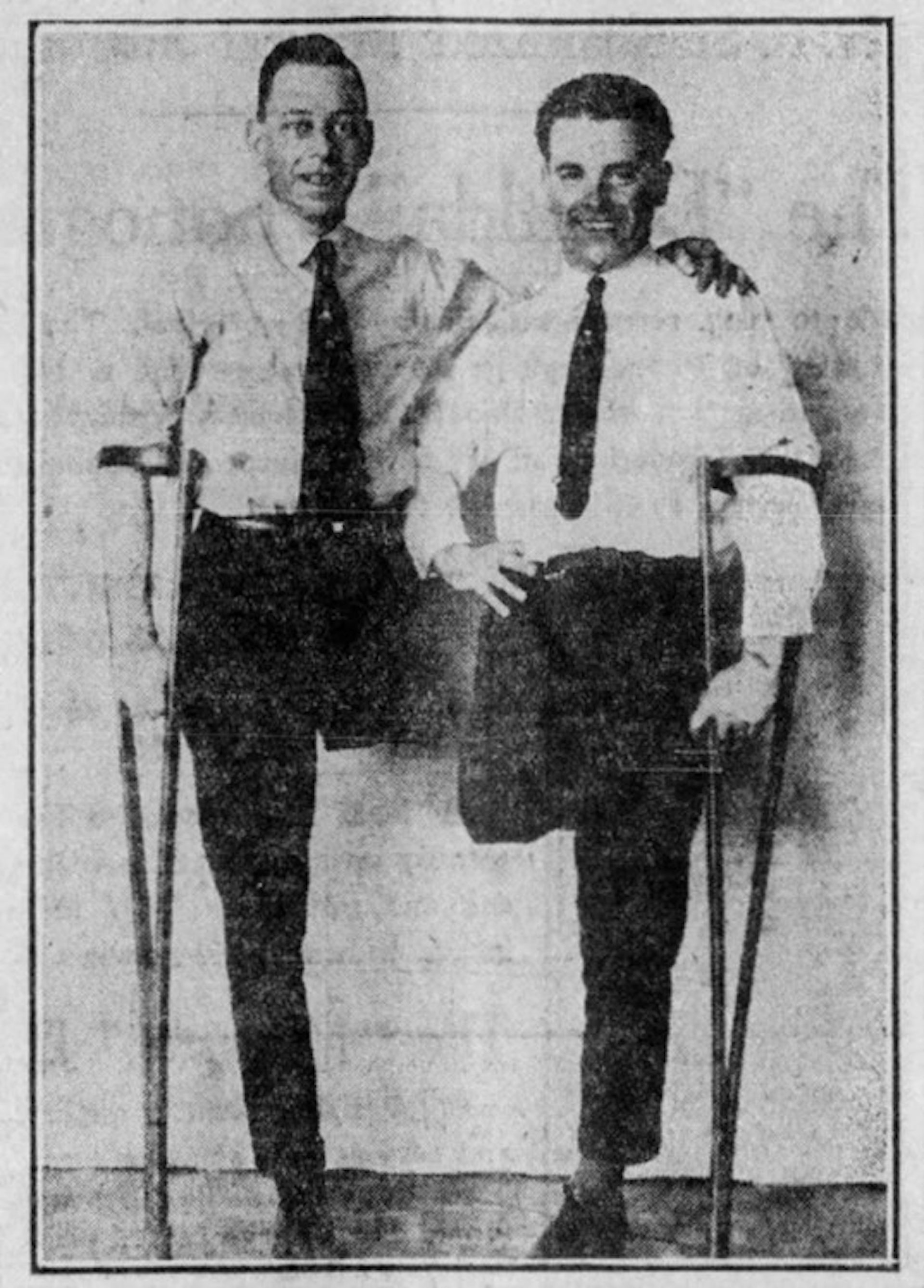 Two men in white shirts and ties and trousers, each having one amputated leg, holding a crutch.