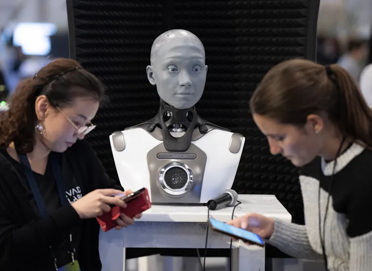 La gente mira sus teléfonos móviles frente al busto del robot
