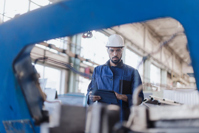 A man in a hard hat looks at the camera through machinery