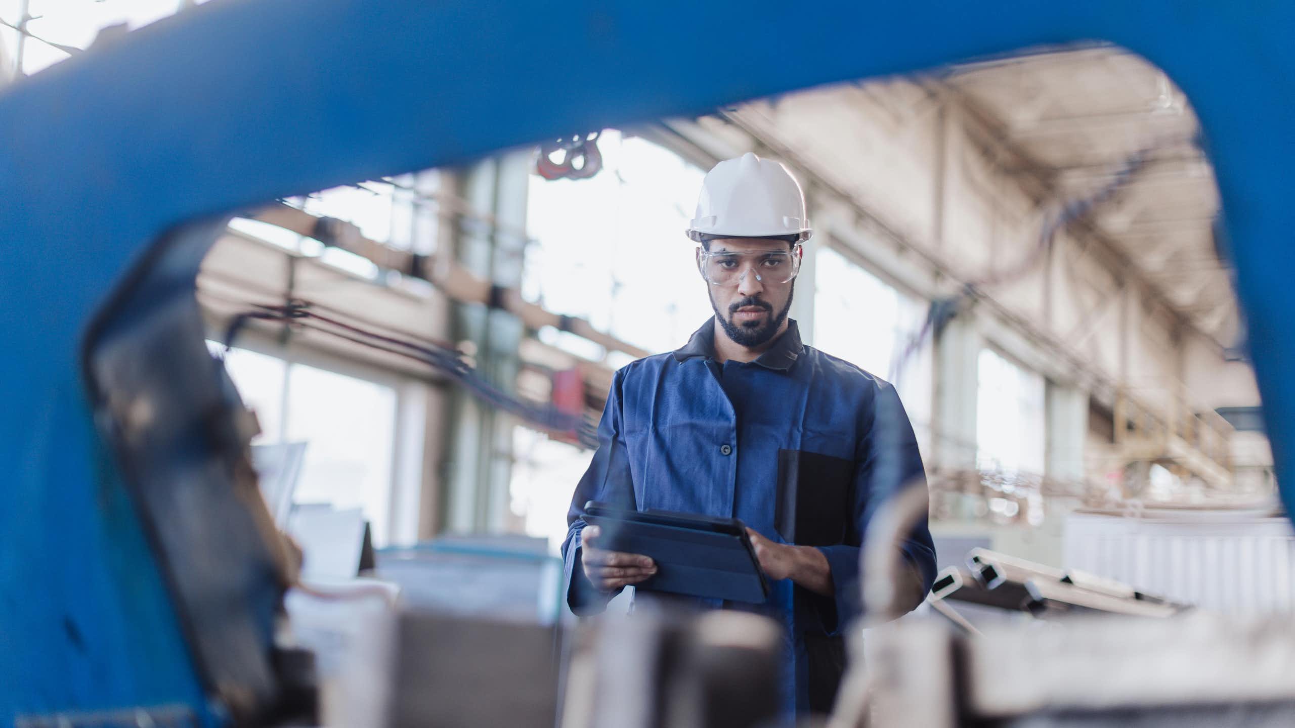A man in a hard hat looks at the camera through machinery