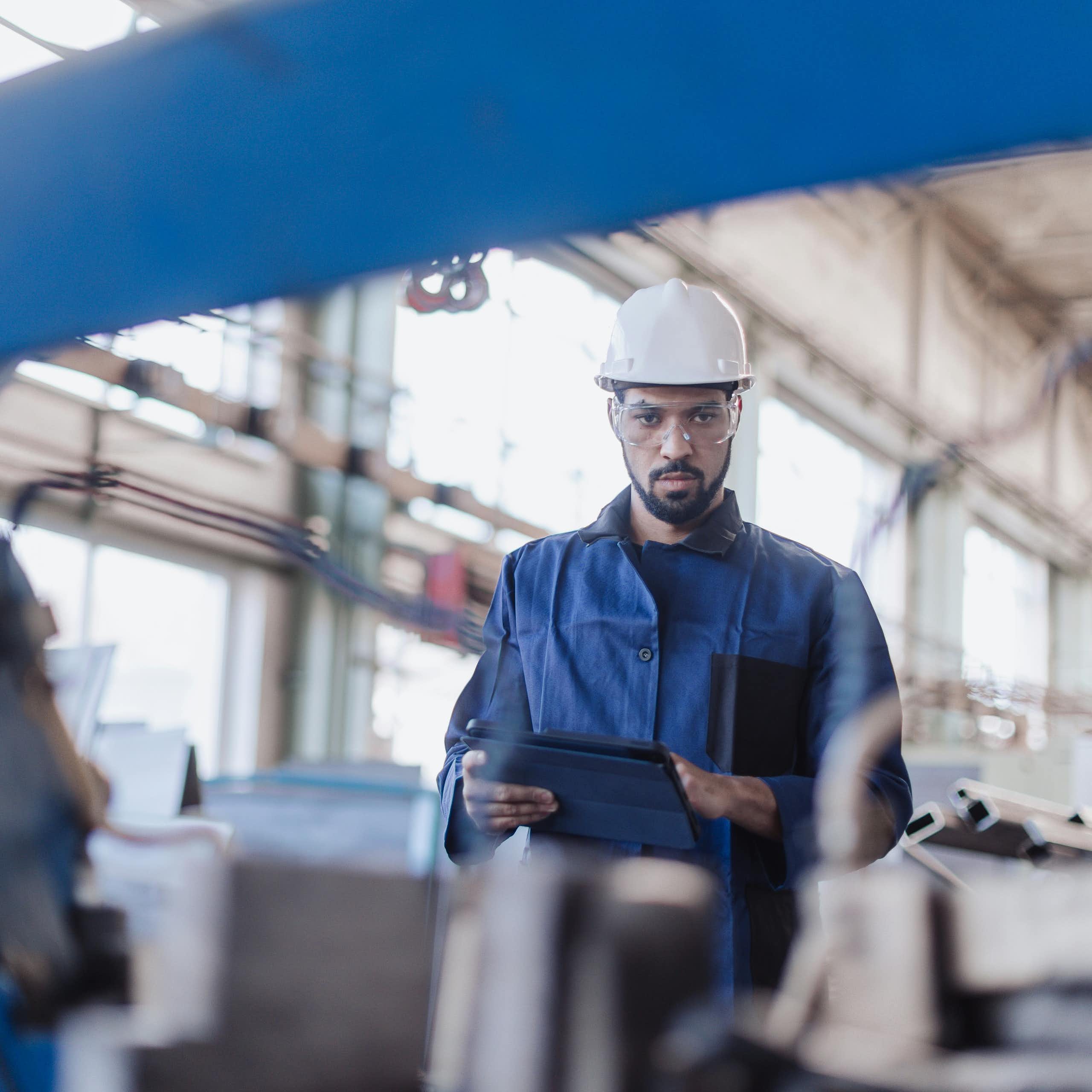 A man in a hard hat looks at the camera through machinery