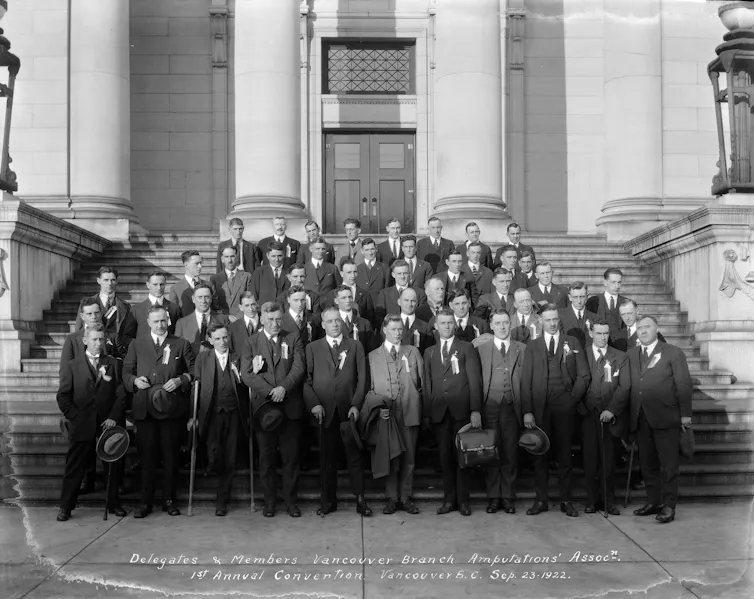 Rows of men standing in suits on steps, many holding one crutch, who have one leg.