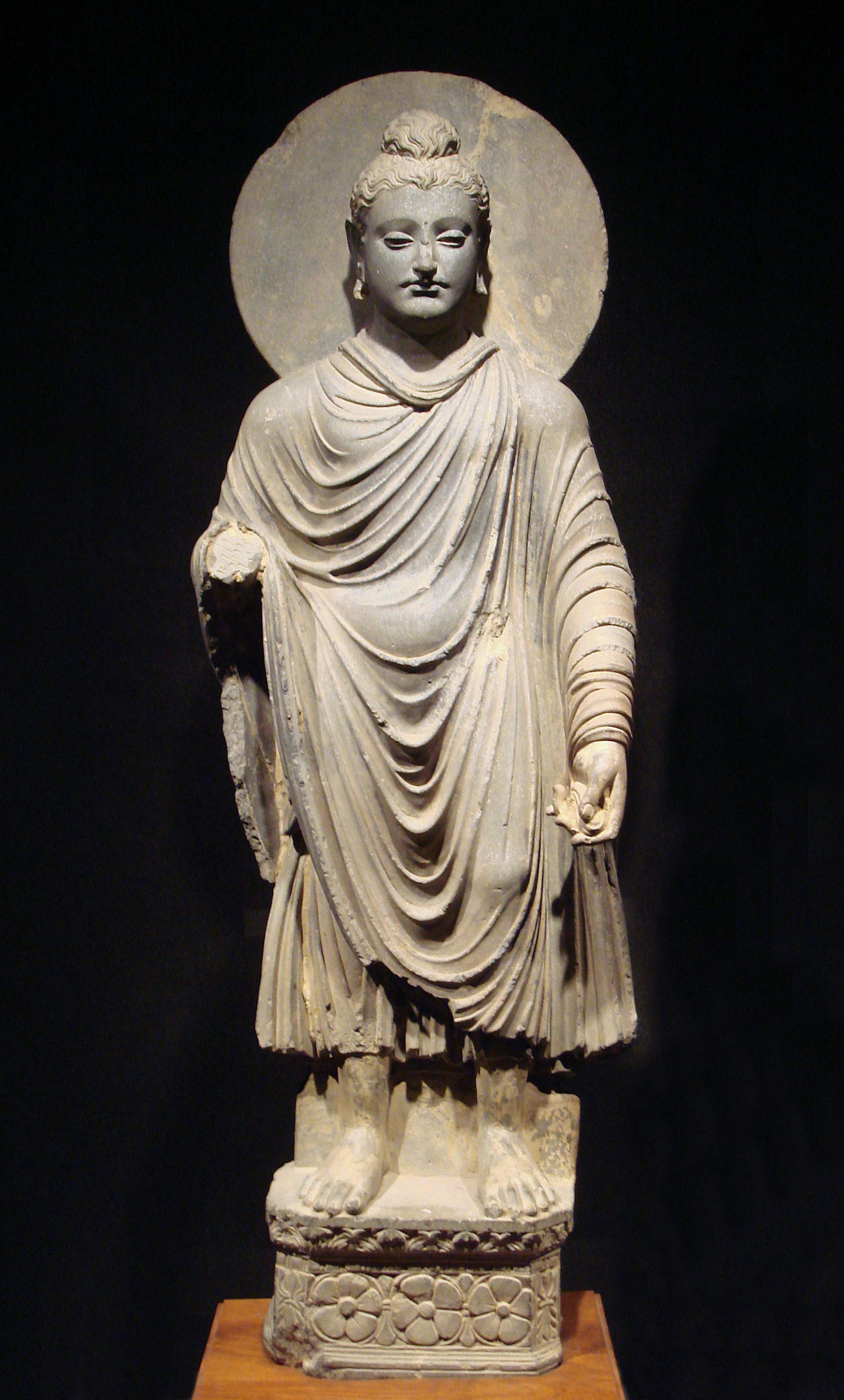 A stone statue of a man with a topknot wearing loosely draped robes, with a circle behind his head.