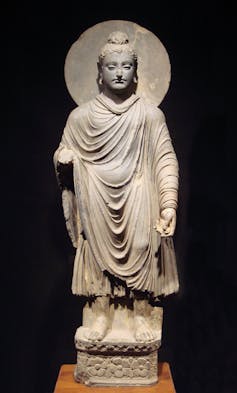 A stone statue of a man with a topknot wearing loosely draped robes, with a circle behind his head.