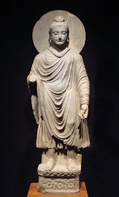 A stone statue of a man with a topknot wearing loosely draped robes, with a circle behind his head.