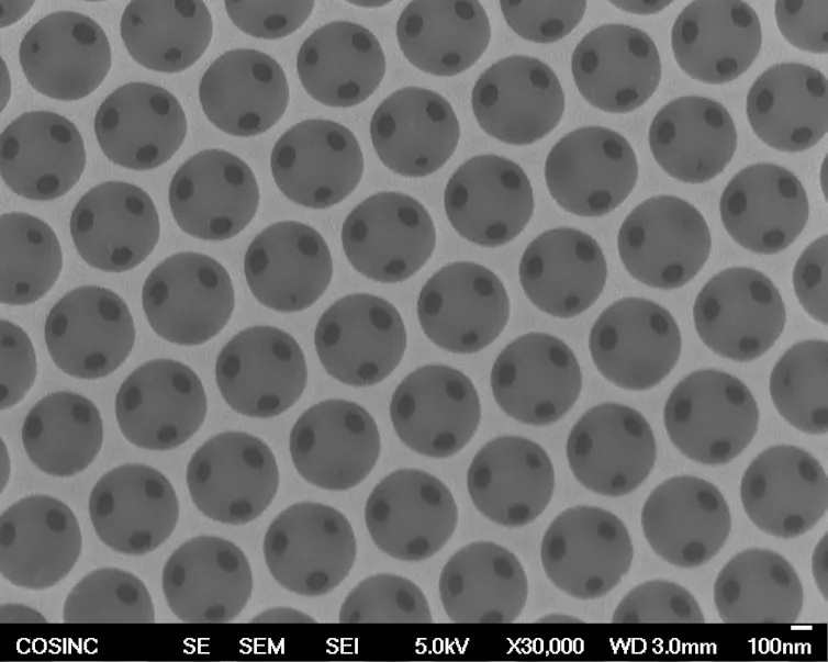 A zoomed in microscope image of a porous material, which is made up of small circles, each with three small cavities, arranged in a grid pattern.