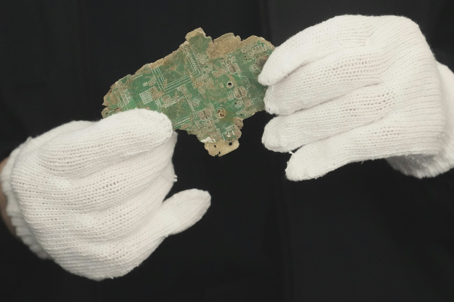 a pair of hands in white gloves holding a broken pieces of a circuit board
