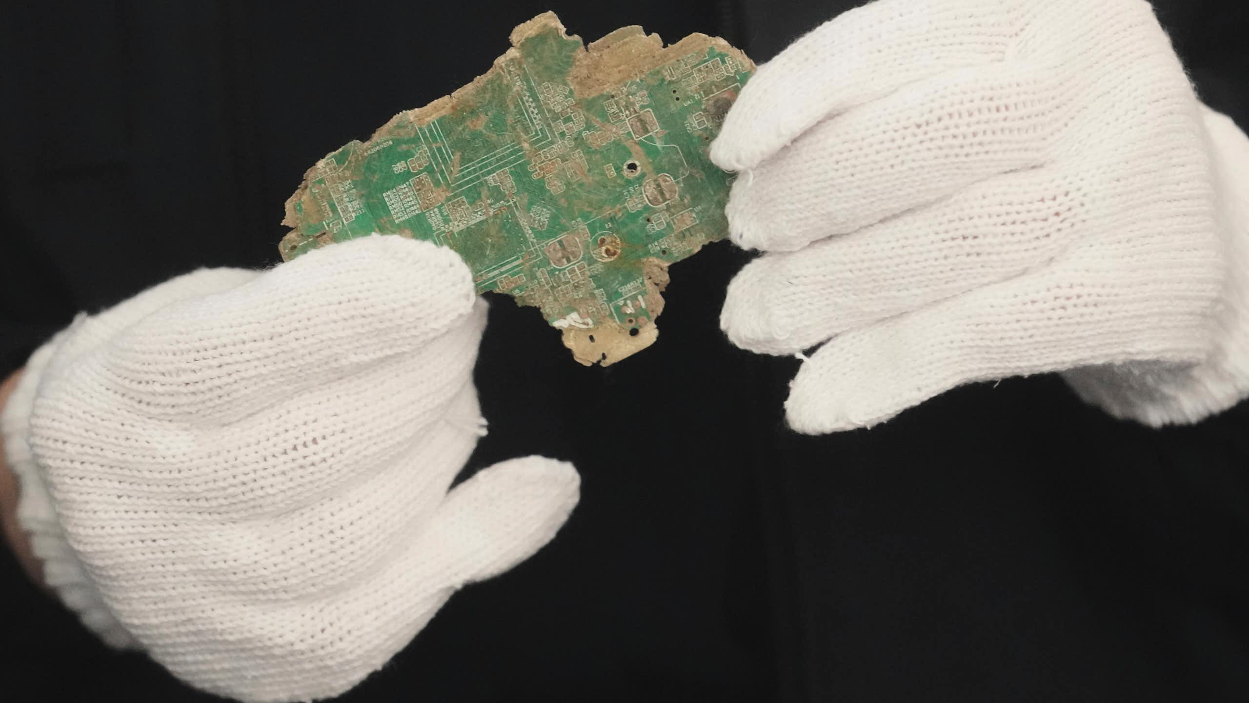 a pair of hands in white gloves holding a broken pieces of a circuit board