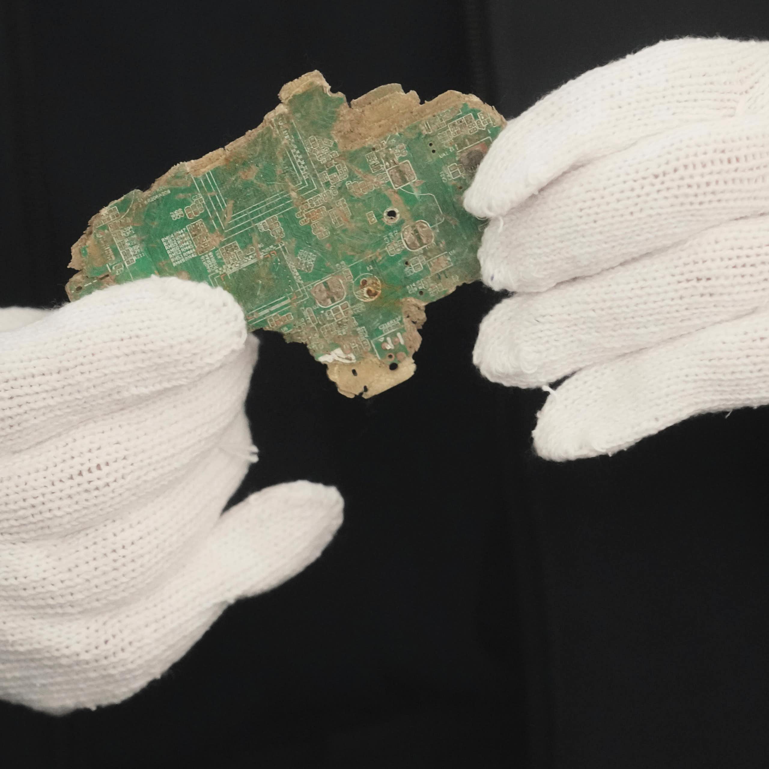 a pair of hands in white gloves holding a broken pieces of a circuit board
