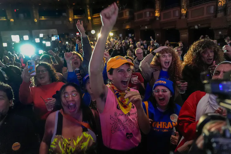 A crowd of people cheer and celebrate in a dimly lit event hall.