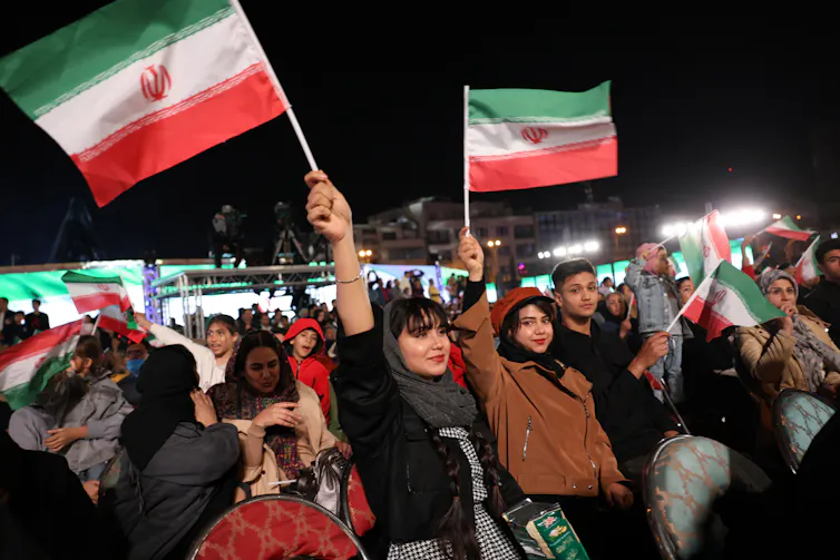 Iranians cheer and wave national flags during a ceremony to unveil a new statue titled 'Kneeling Before Iran' at the Enghelab Square, in Tehran, Iran