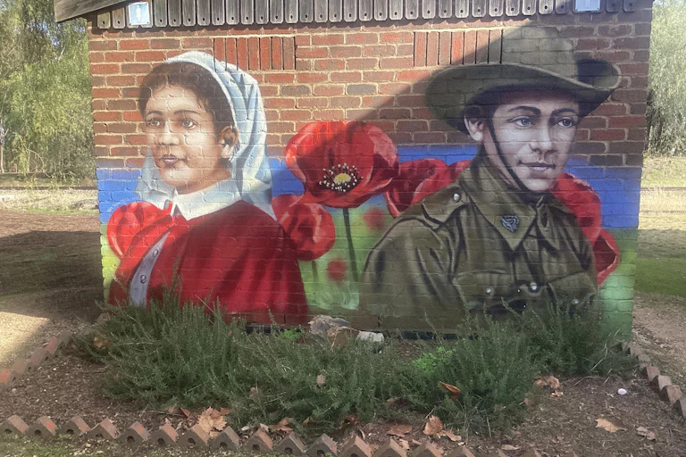 An ANZAC mural is painted on a toilet block, with red flowers and two figures.