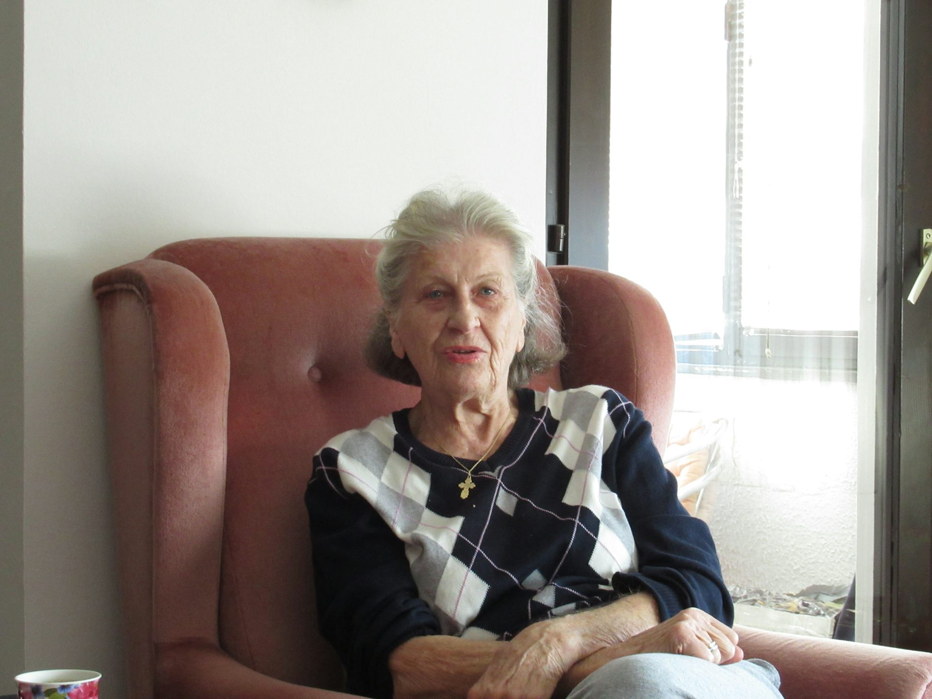 An older woman sits in an armchair next to a window