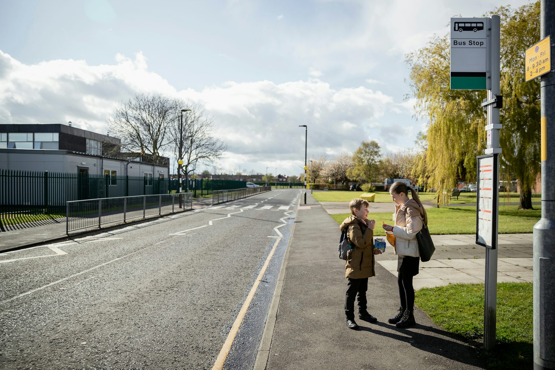 A young boy and girl waiting at a bus stop on an empty suburban road