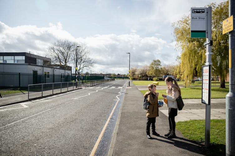 A young boy and girl waiting at a bus stop on an empty suburban road