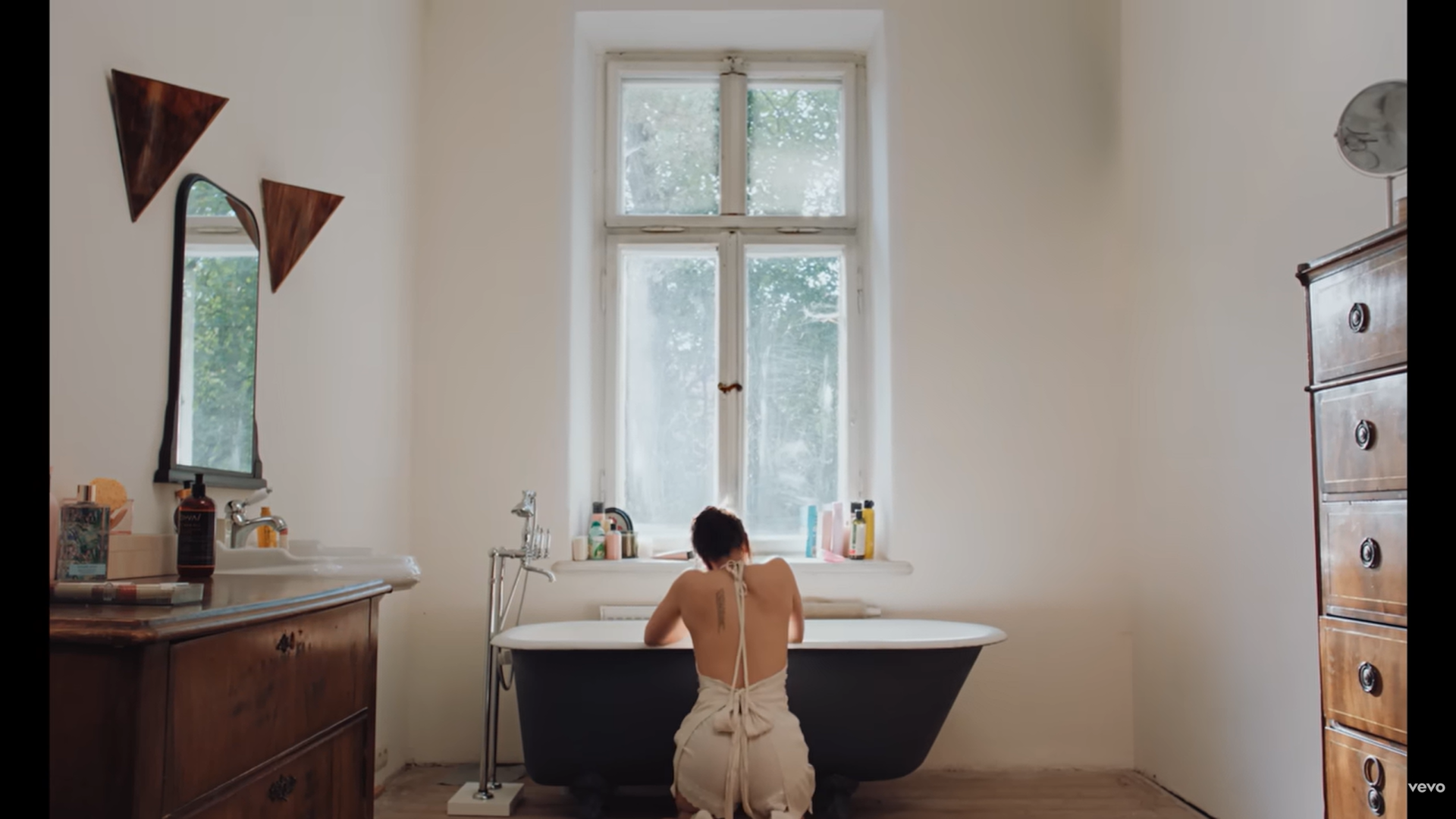 Una mujer de rodillas frente a una bañera, de espaldas a la cámara.