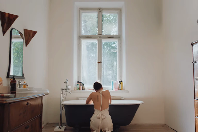 Una mujer de rodillas frente a una bañera, de espaldas a la cámara.