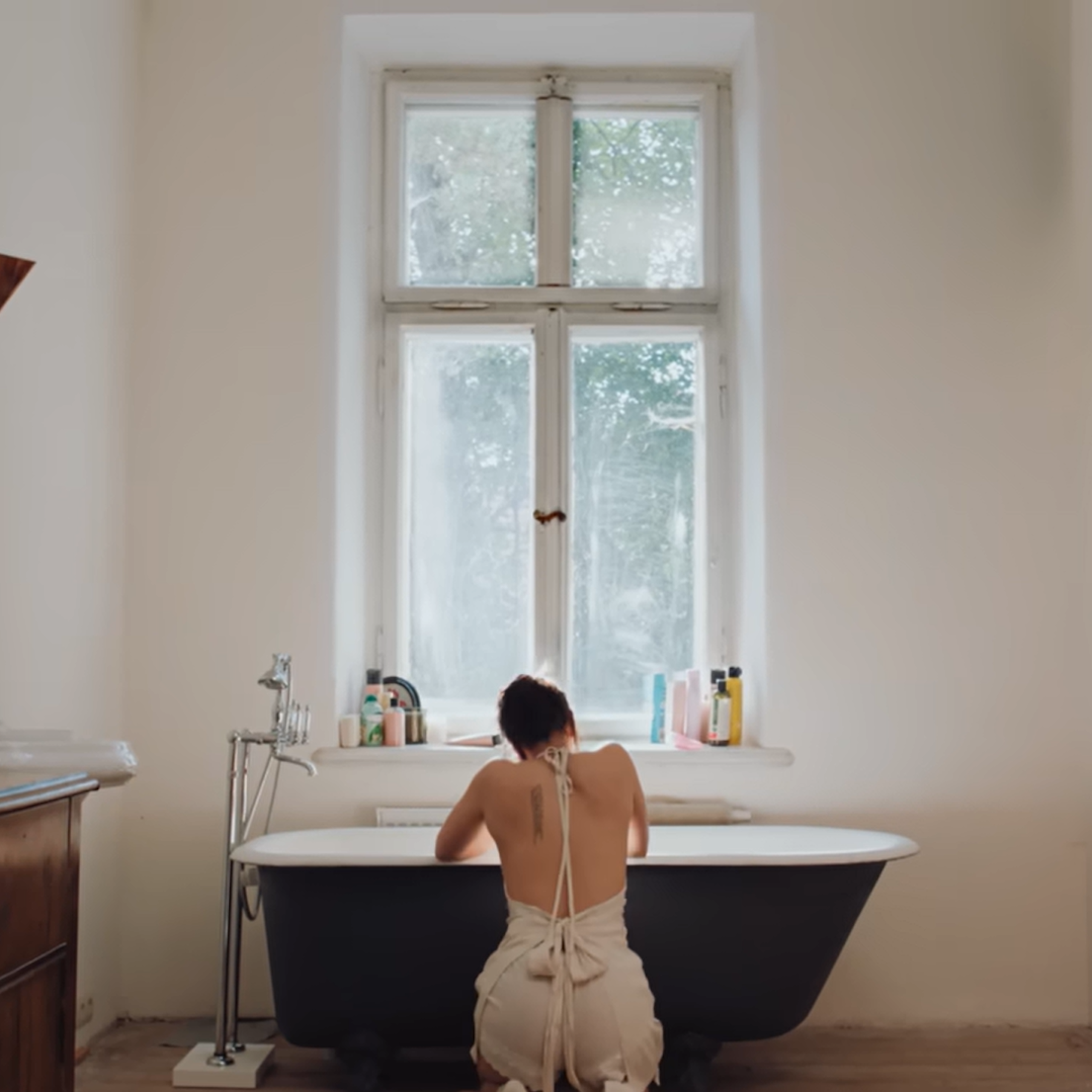 Una mujer de rodillas frente a una bañera, de espaldas a la cámara.