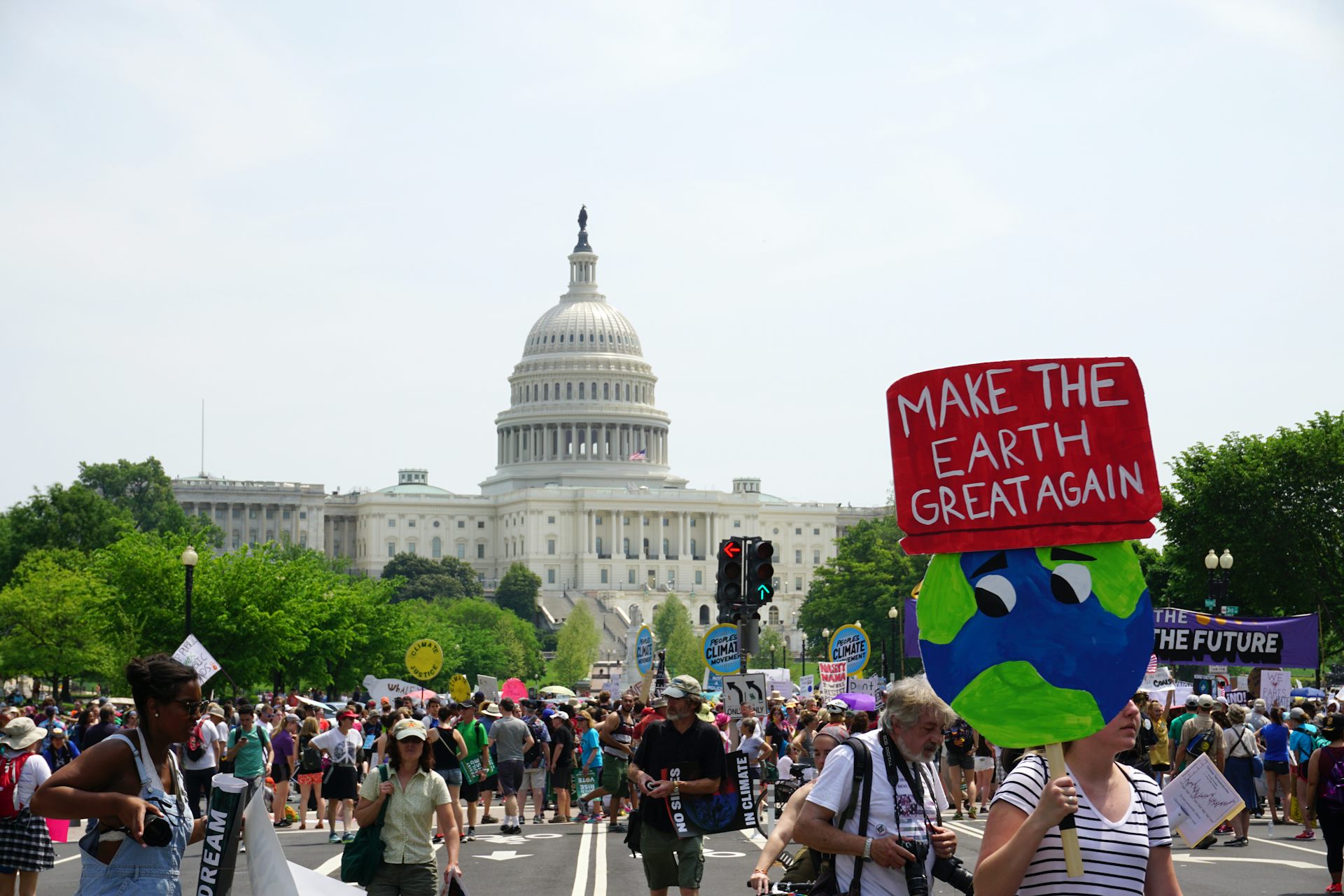 A protester with sign saying 'make the earth great again' marches in front of the US capitol.