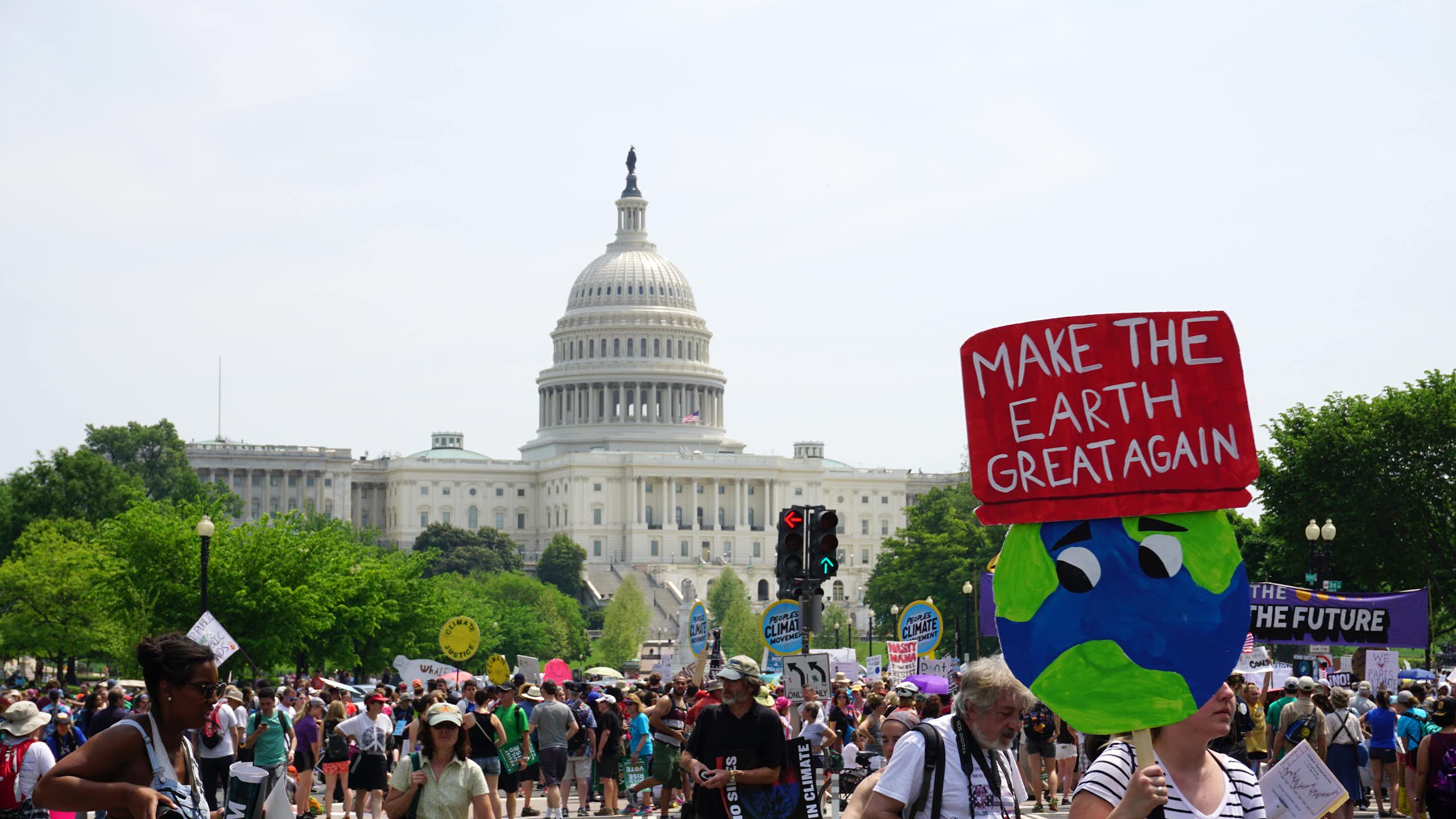A protester with sign saying 'make the earth great again' marches in front of the US capitol.