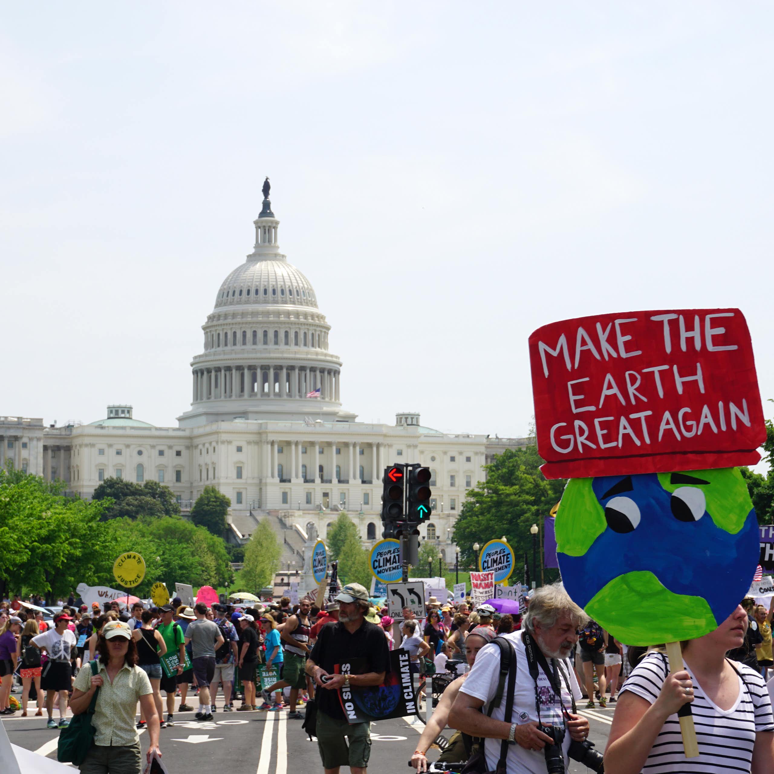 A protester with sign saying 'make the earth great again' marches in front of the US capitol.