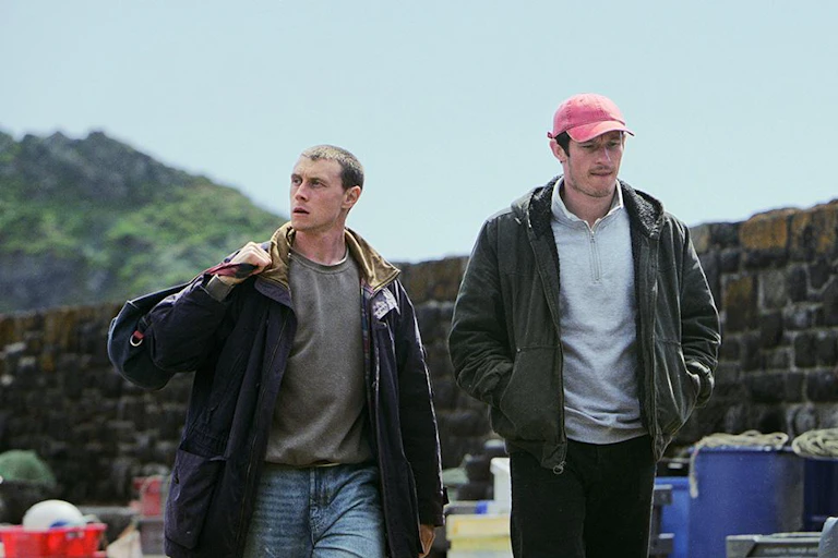 George MacKay and Callum Turner walking in a fishing village