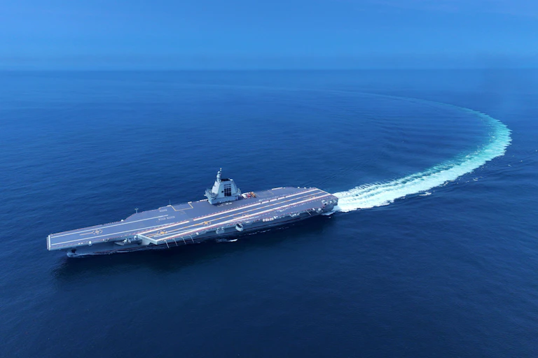 A large Chinese aircraft6 carrier performing a turn, shoning a long wake.
