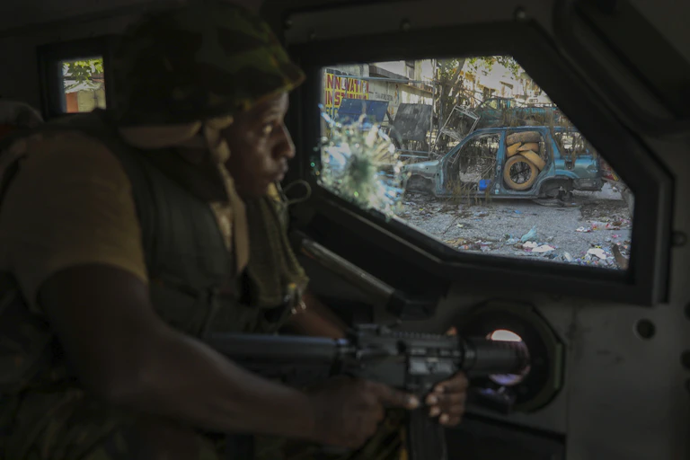 A soldier looks out a window at a trash-strewn street.
