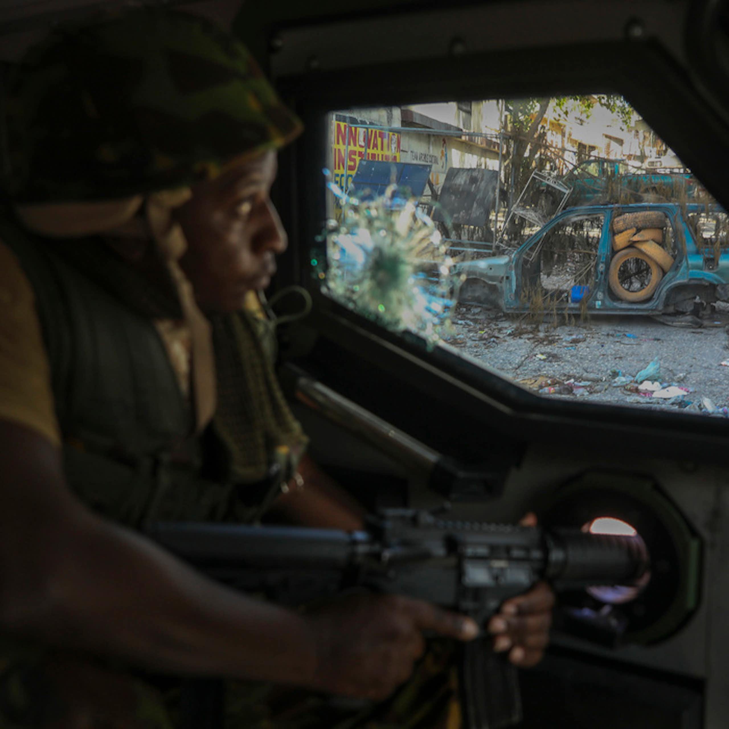 A soldier looks out a window at a trash-strewn street.