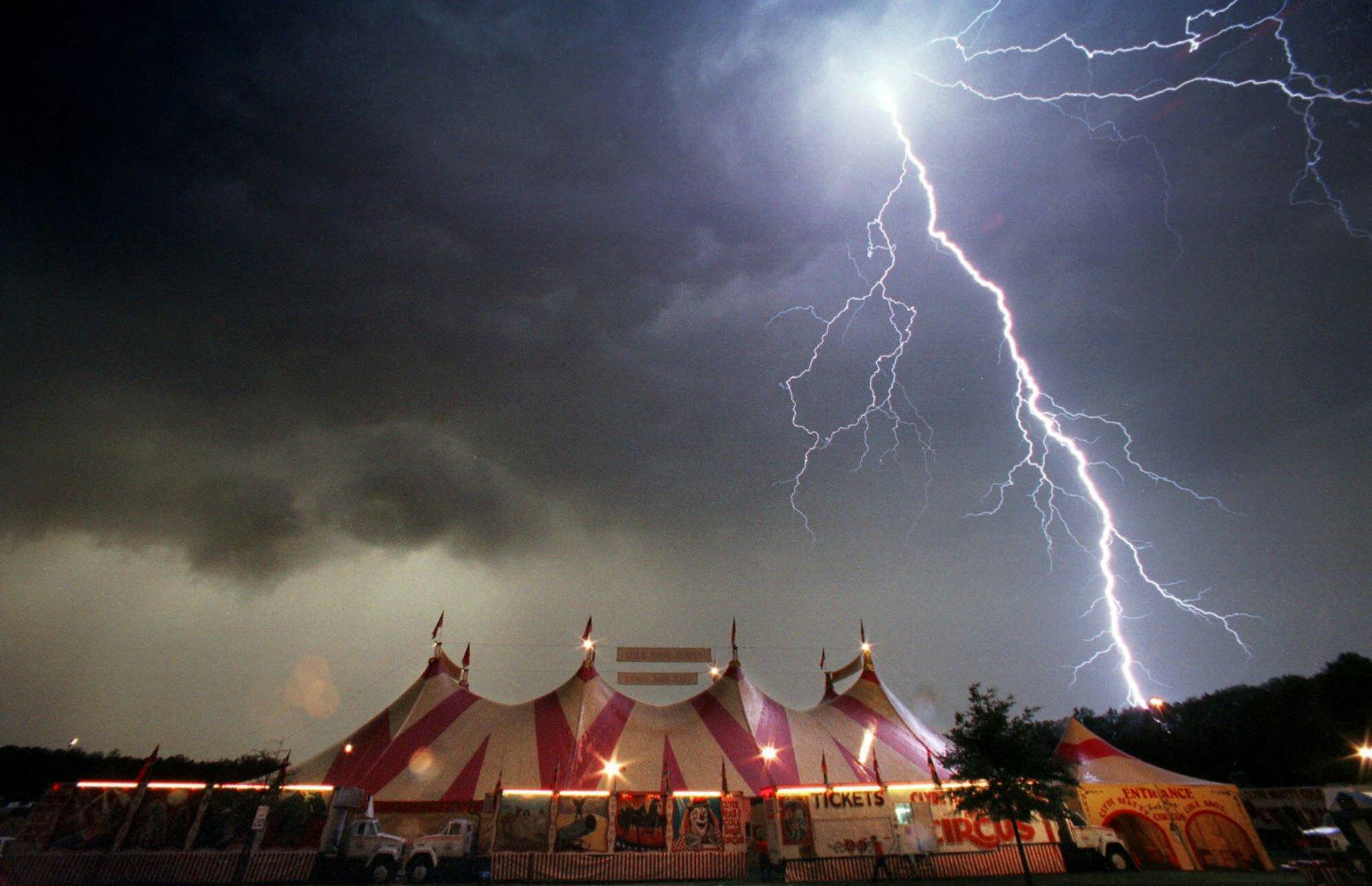 A dark sky and lightning seen over a circus tent.