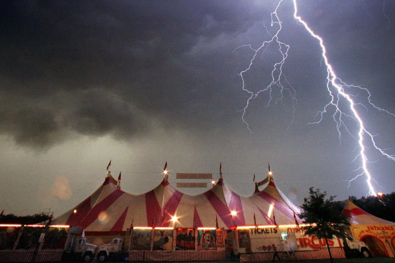 A dark sky and lightning seen over a circus tent.