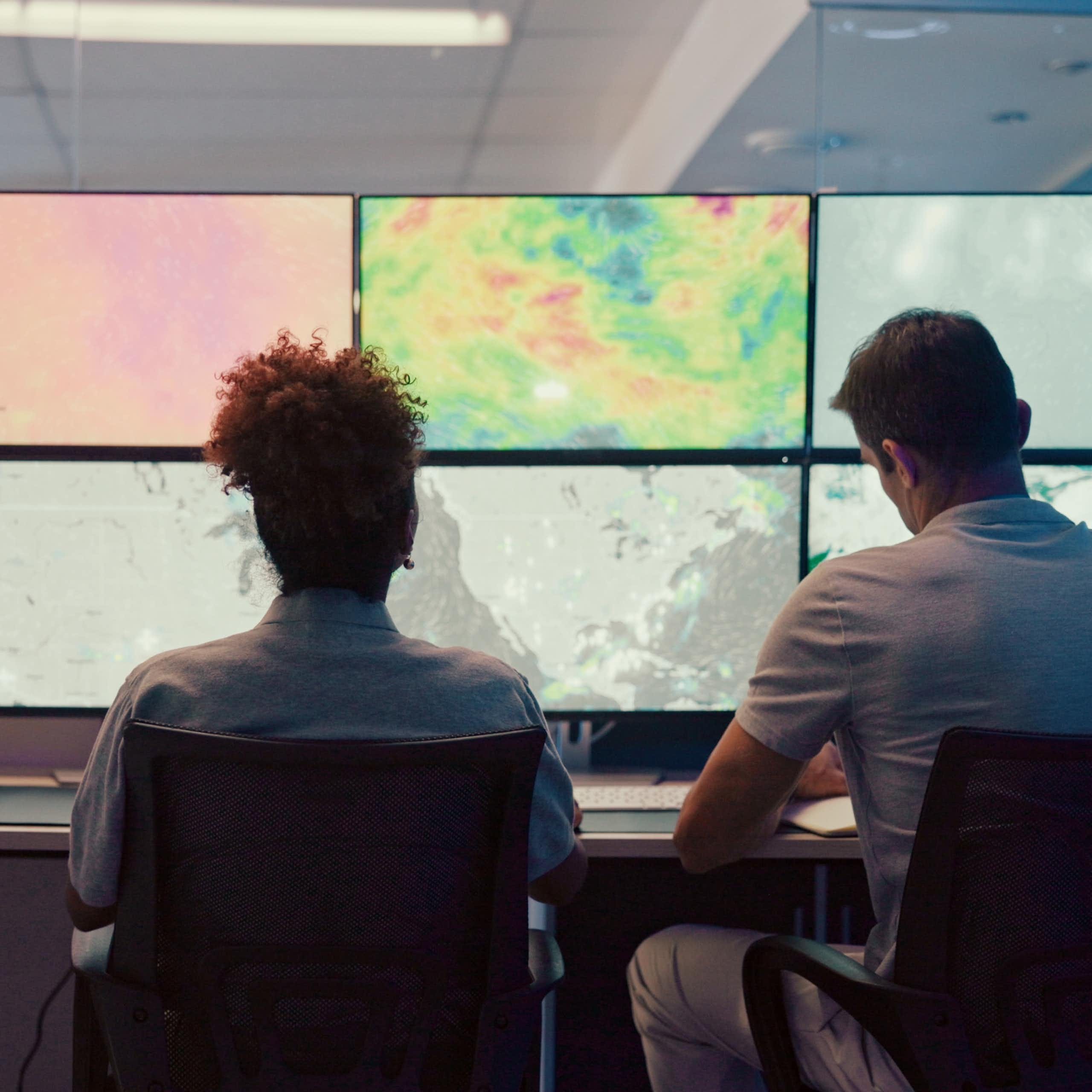 Trois personnes assises devant des écrans d'ordinateur présentant différentes cartes météorologiques.