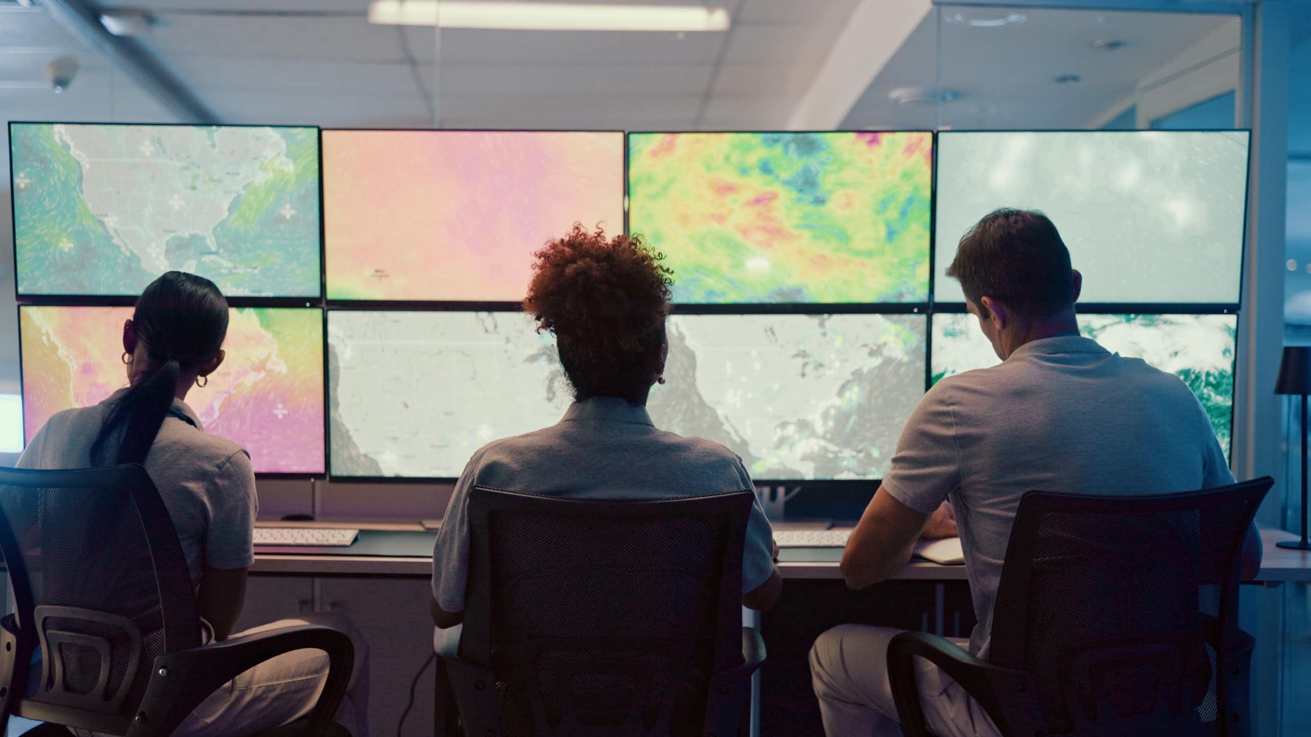 Trois personnes assises devant des écrans d'ordinateur présentant différentes cartes météorologiques.