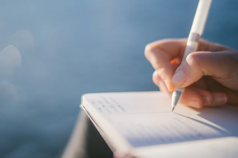 Close-up of hand writing in notebook with pen