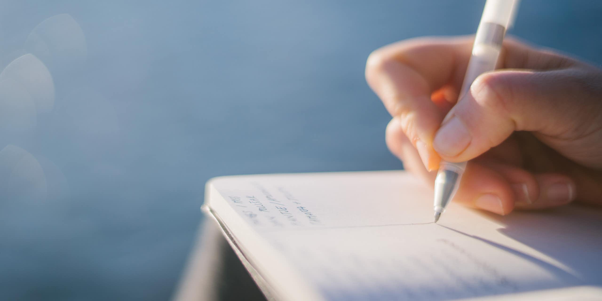 Close-up of hand writing in notebook with pen