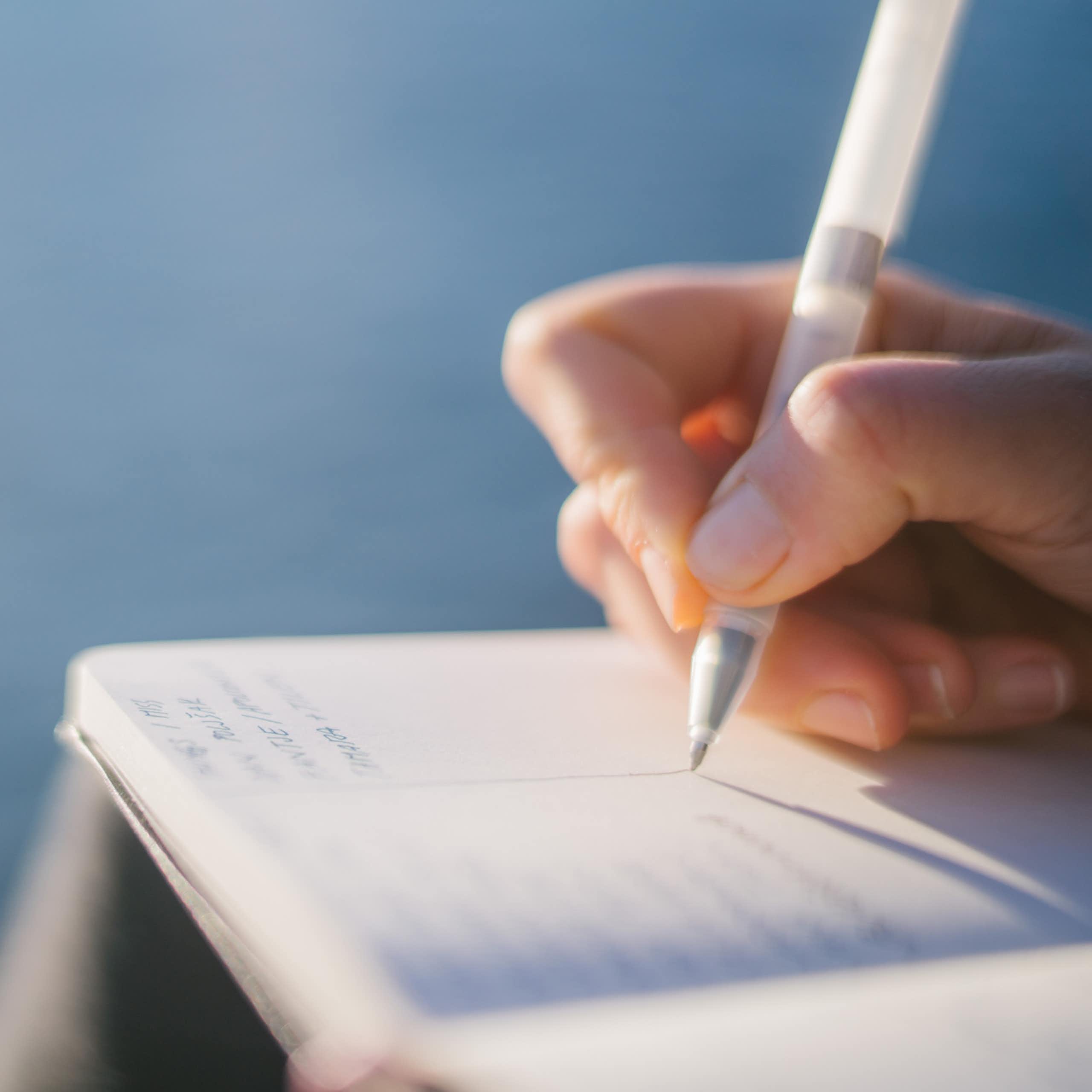 Close-up of hand writing in notebook with pen