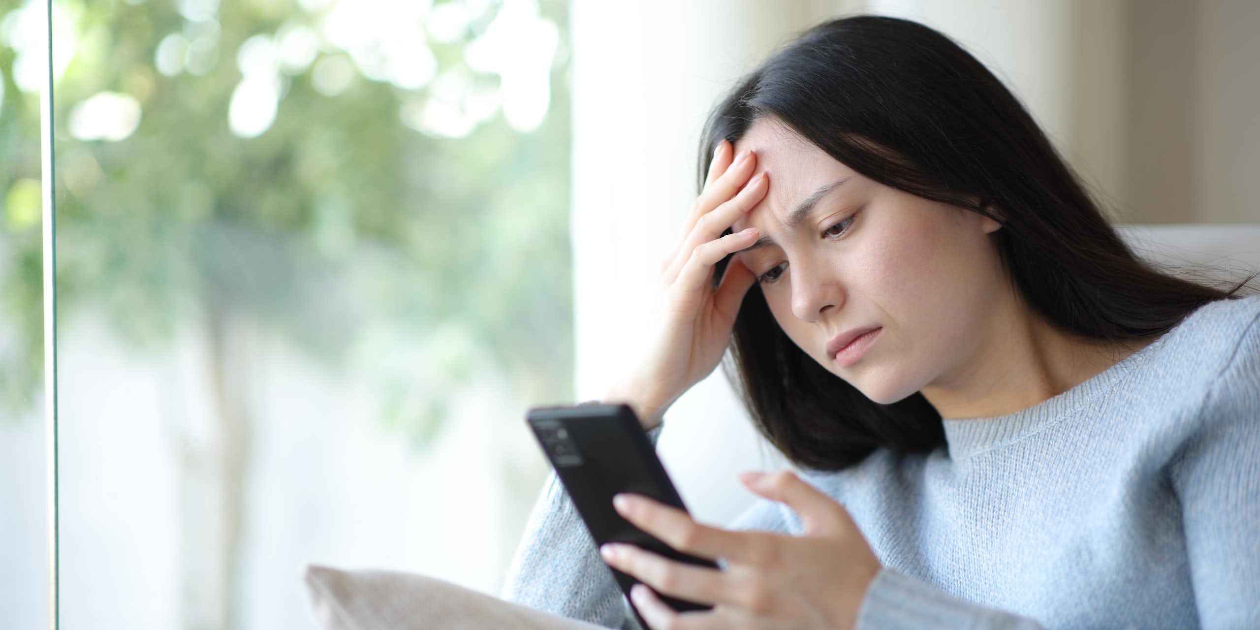woman looking at her phone with a furrowed brow
