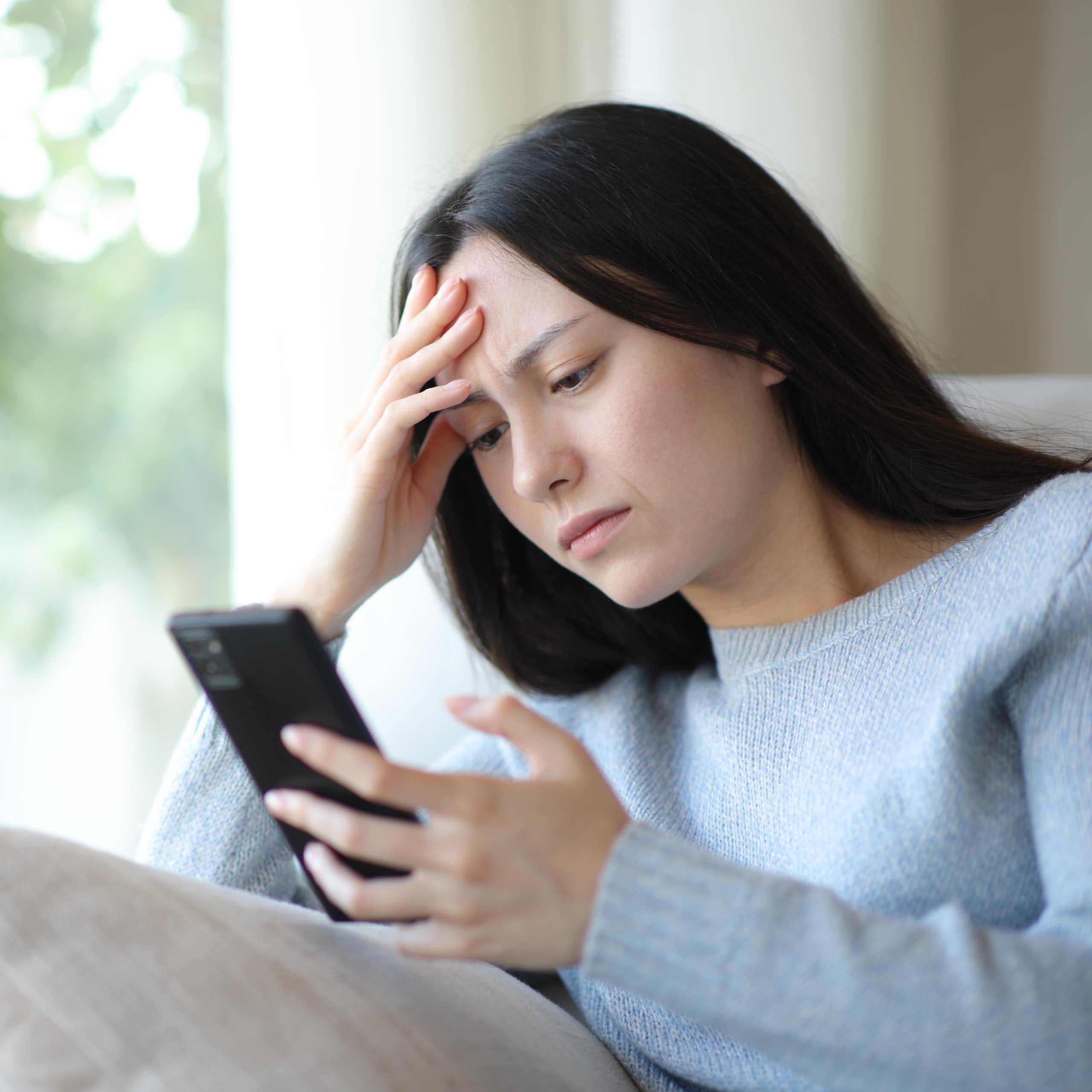 woman looking at her phone with a furrowed brow