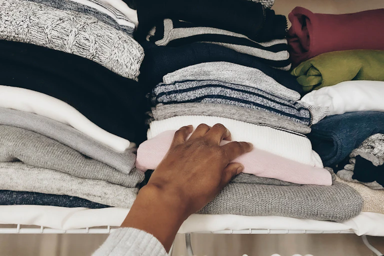A person reaches for a sweater in a pile of clothing.