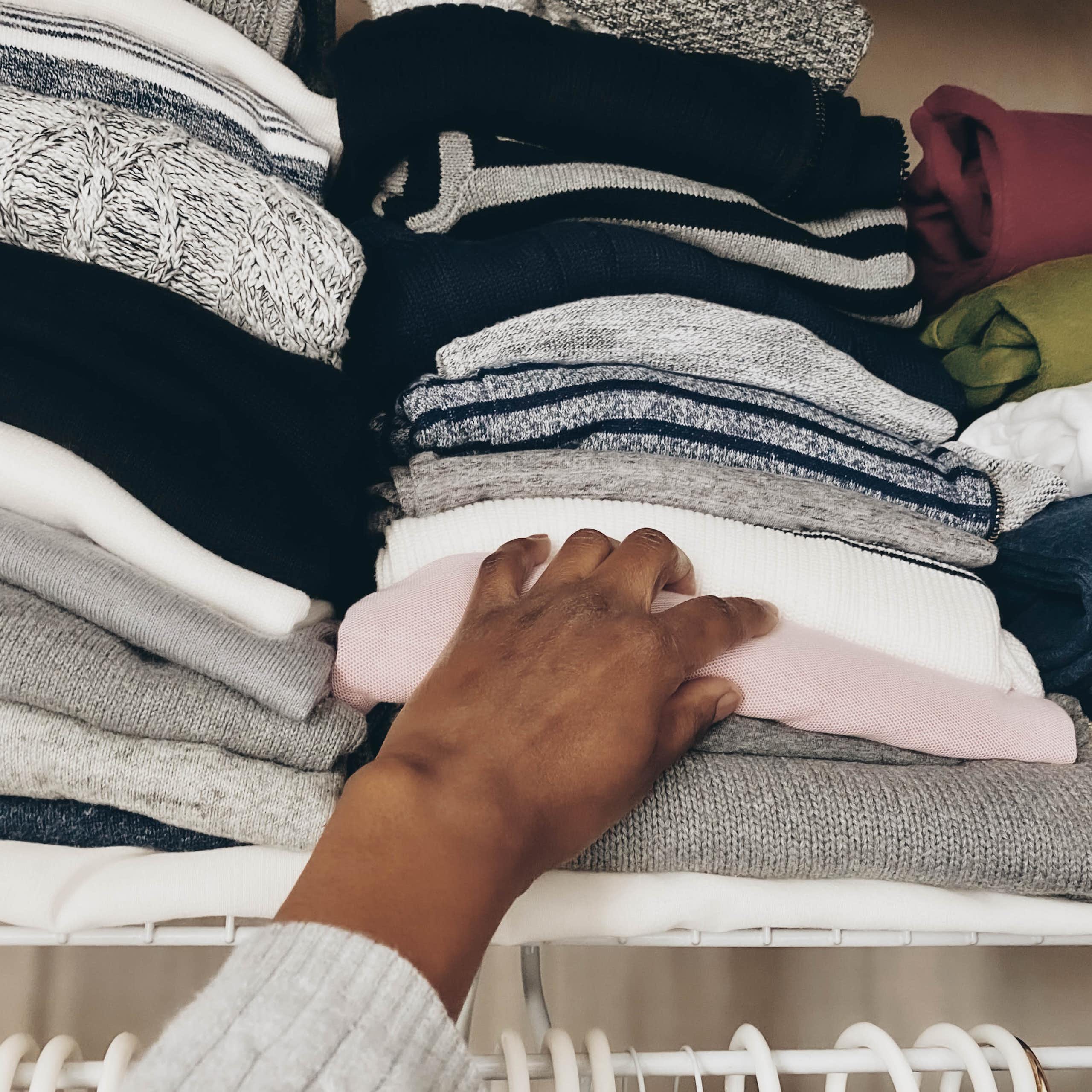 A person reaches for a sweater in a pile of clothing.